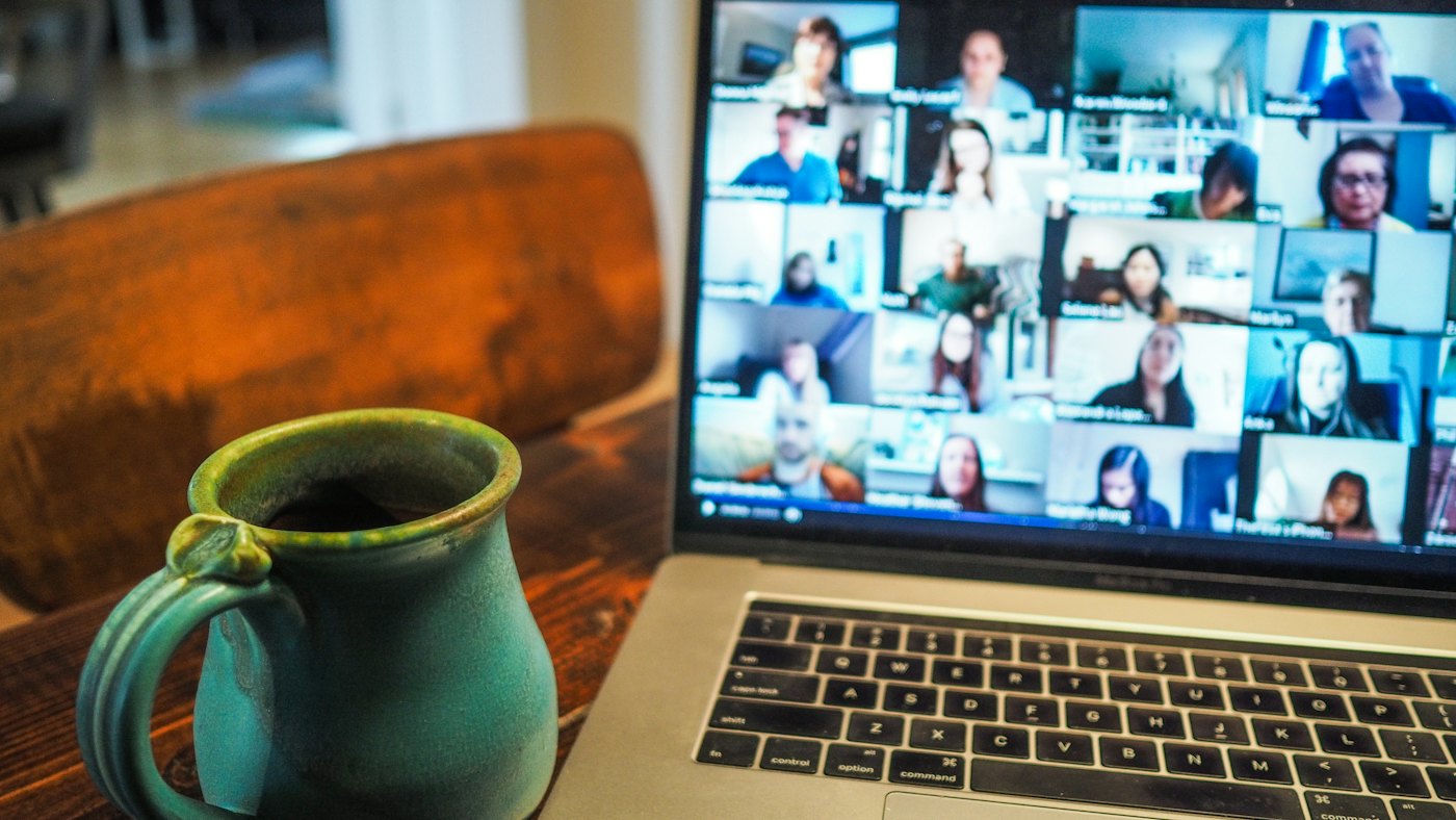 Laptop showing a video call with many participants next to a coffee mug
