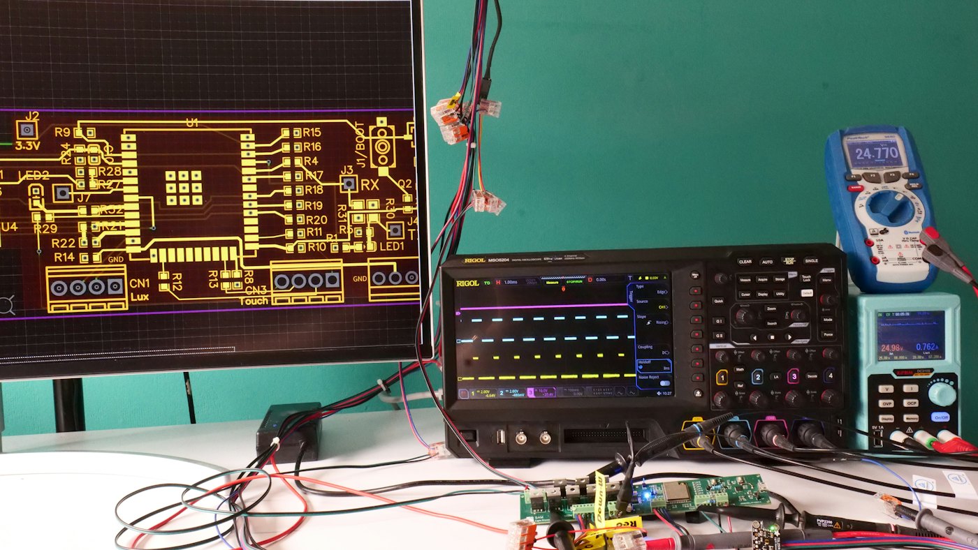 Electronics bench with a PCB layout on screen, an oscilloscope and a multimeter