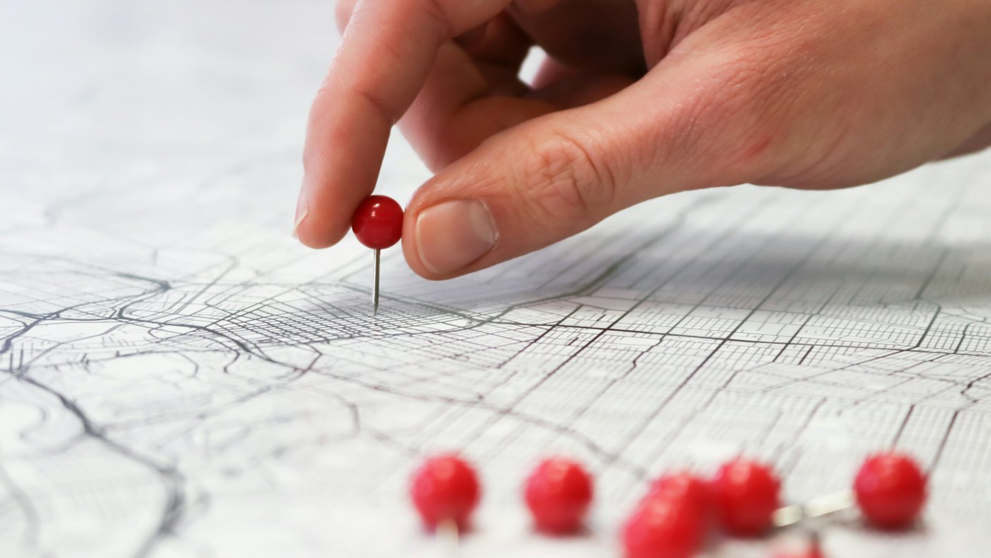 Hand placing a red pin on a printed street map
