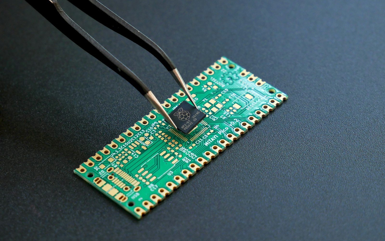 Tweezers placing a microchip onto a green circuit board